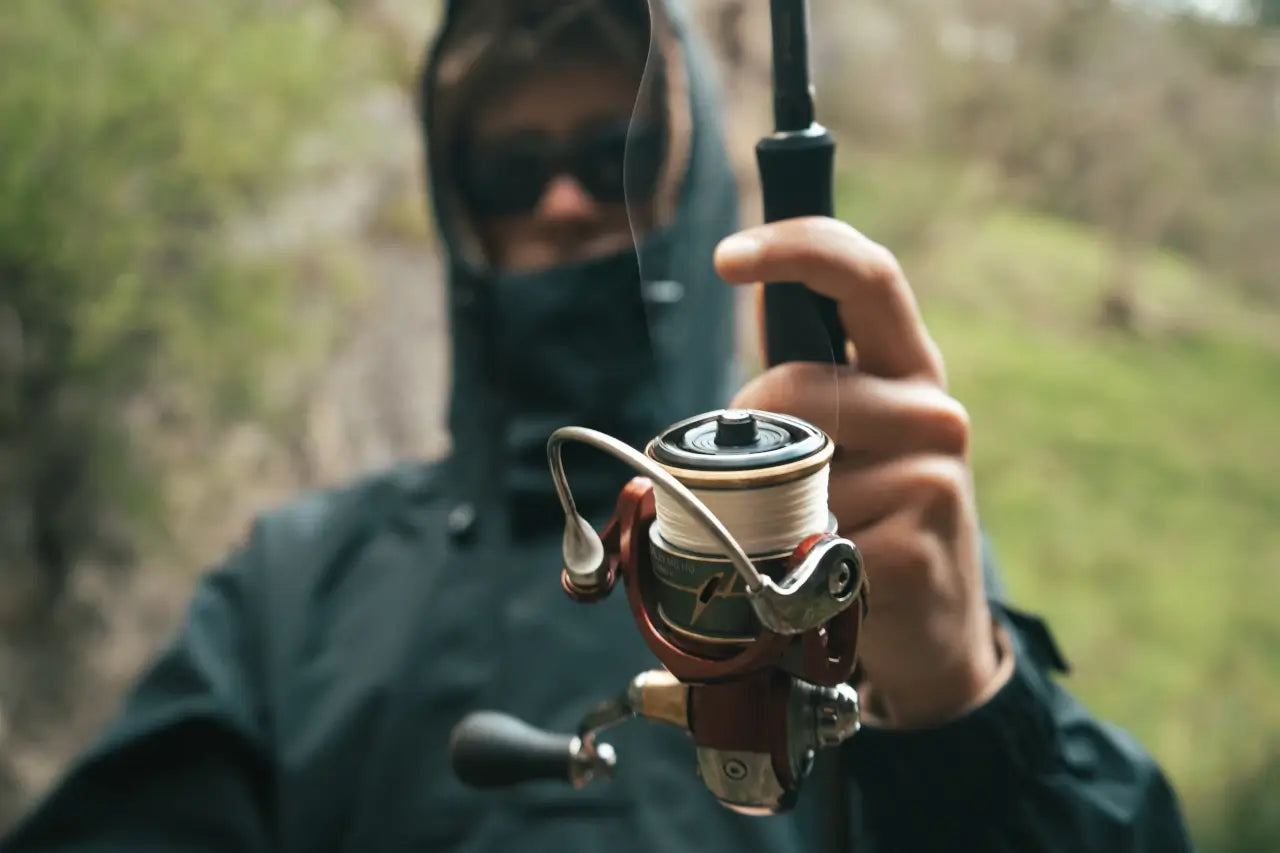 Angler in sunglasses holding a spinning reel with a thumb on the spool, braid running off it