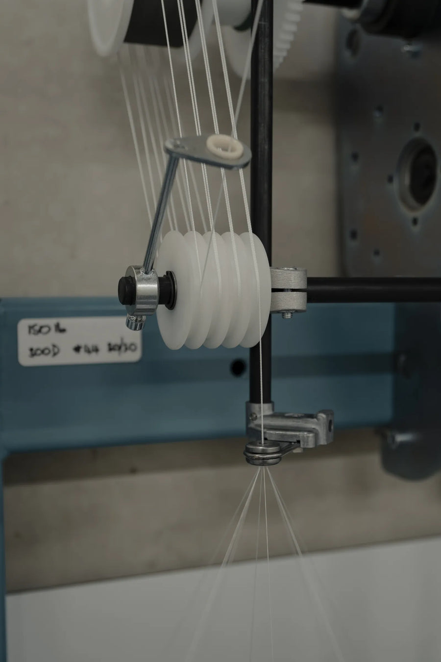 Braiding machine carrier with a white yarn bobbin, fine strands fanning out towards the braiding point