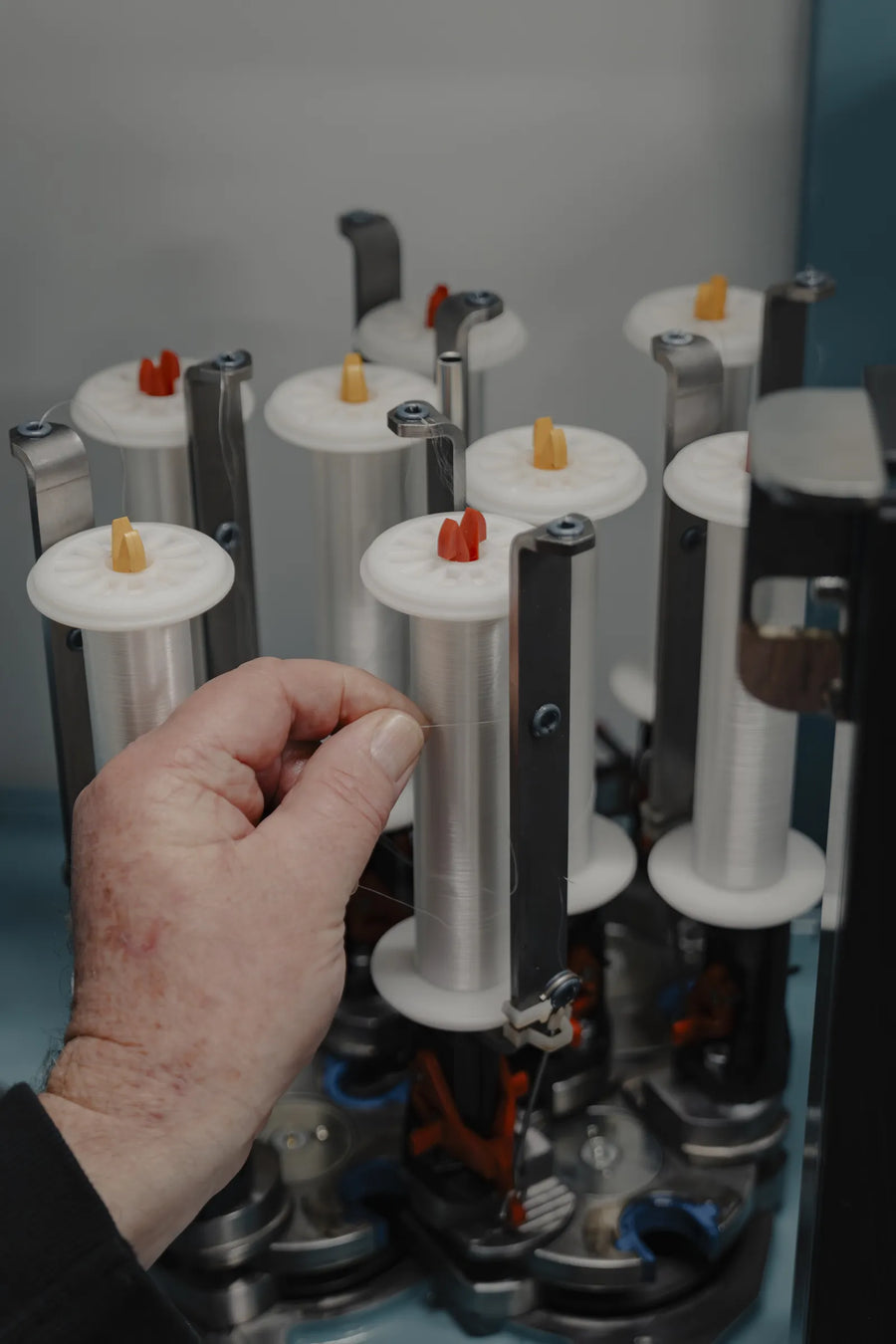 Hand loading a white yarn bobbin onto a creel stand of spools in the Tasline factory