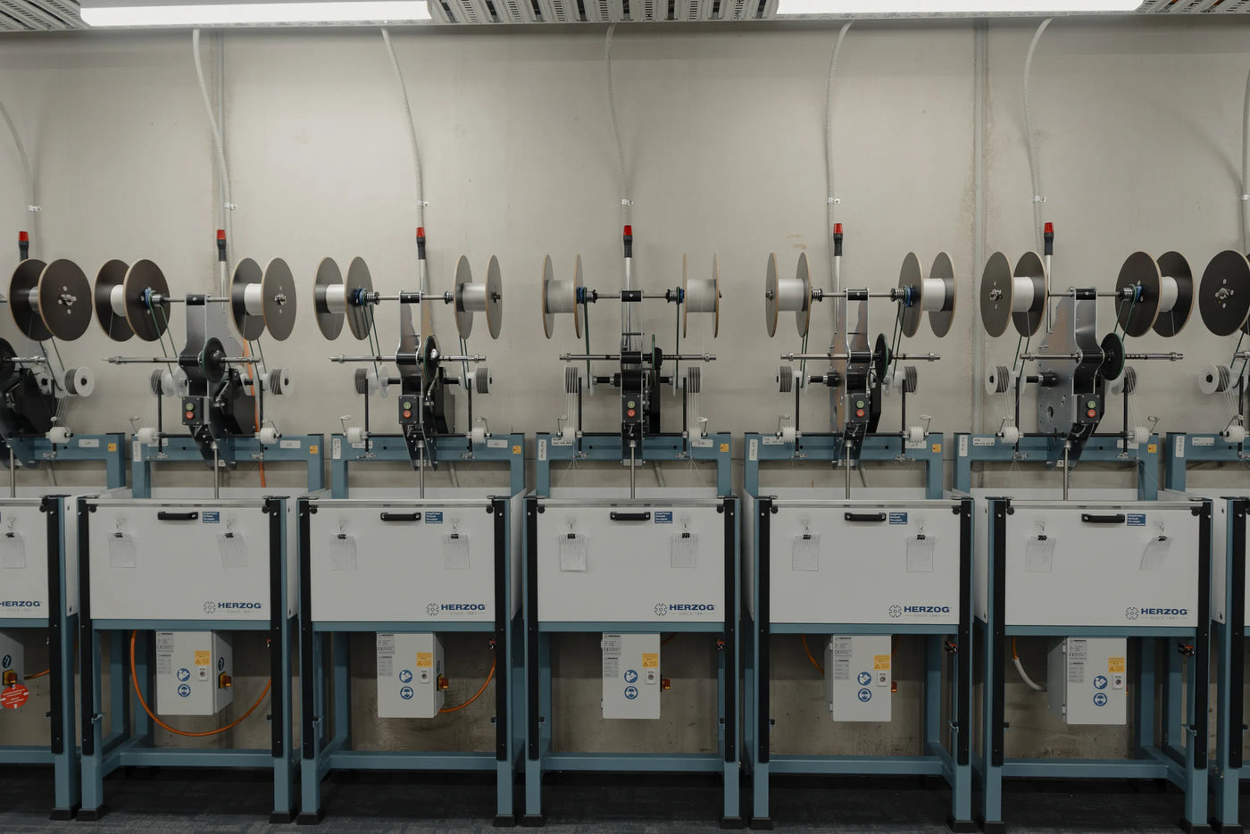 Herzog braiding machines photographed head-on in a row, white carrier spools mounted across each machine